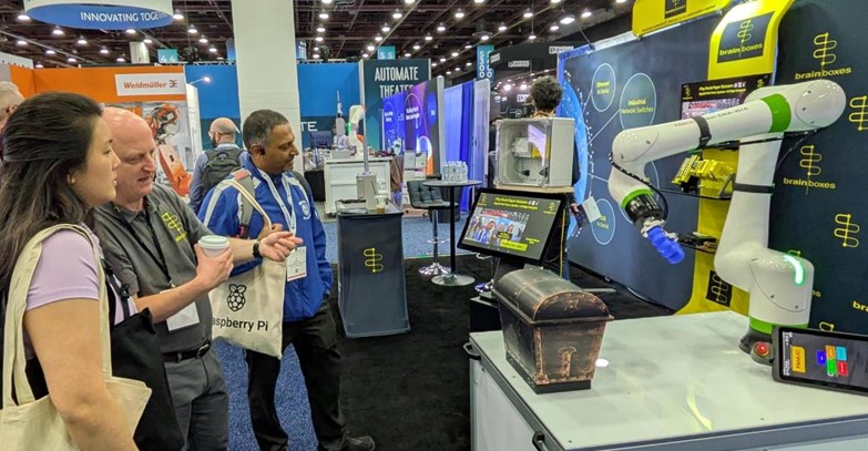 People interact with a robot arm, AI vision systems demo shown on a touchscreen